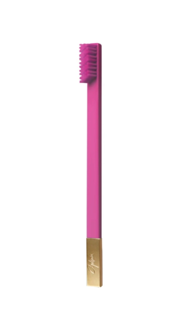 A bubblegum pink toothbrush with a gold-colored handle and soft bristles.