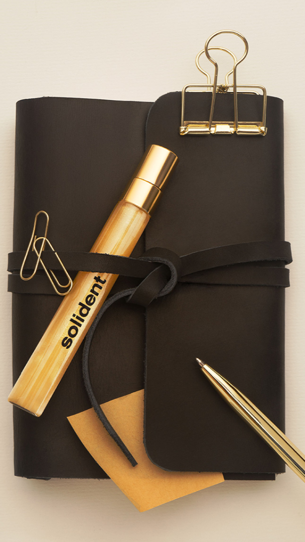 Black notebook with gold pen and clips on a beige background