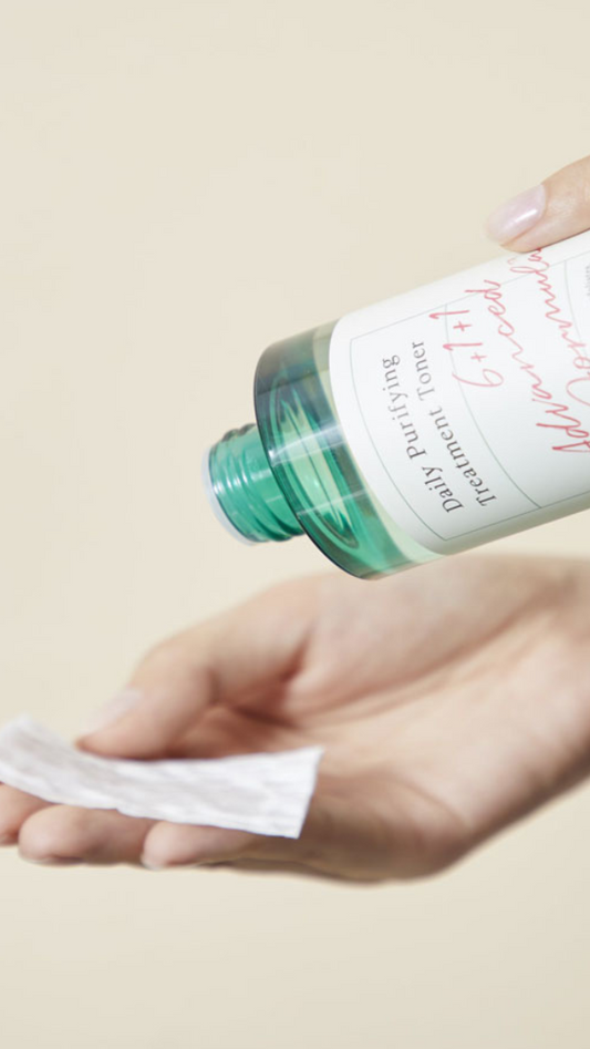 Hand holding a bottle of facial toner and a cotton pad on a beige background