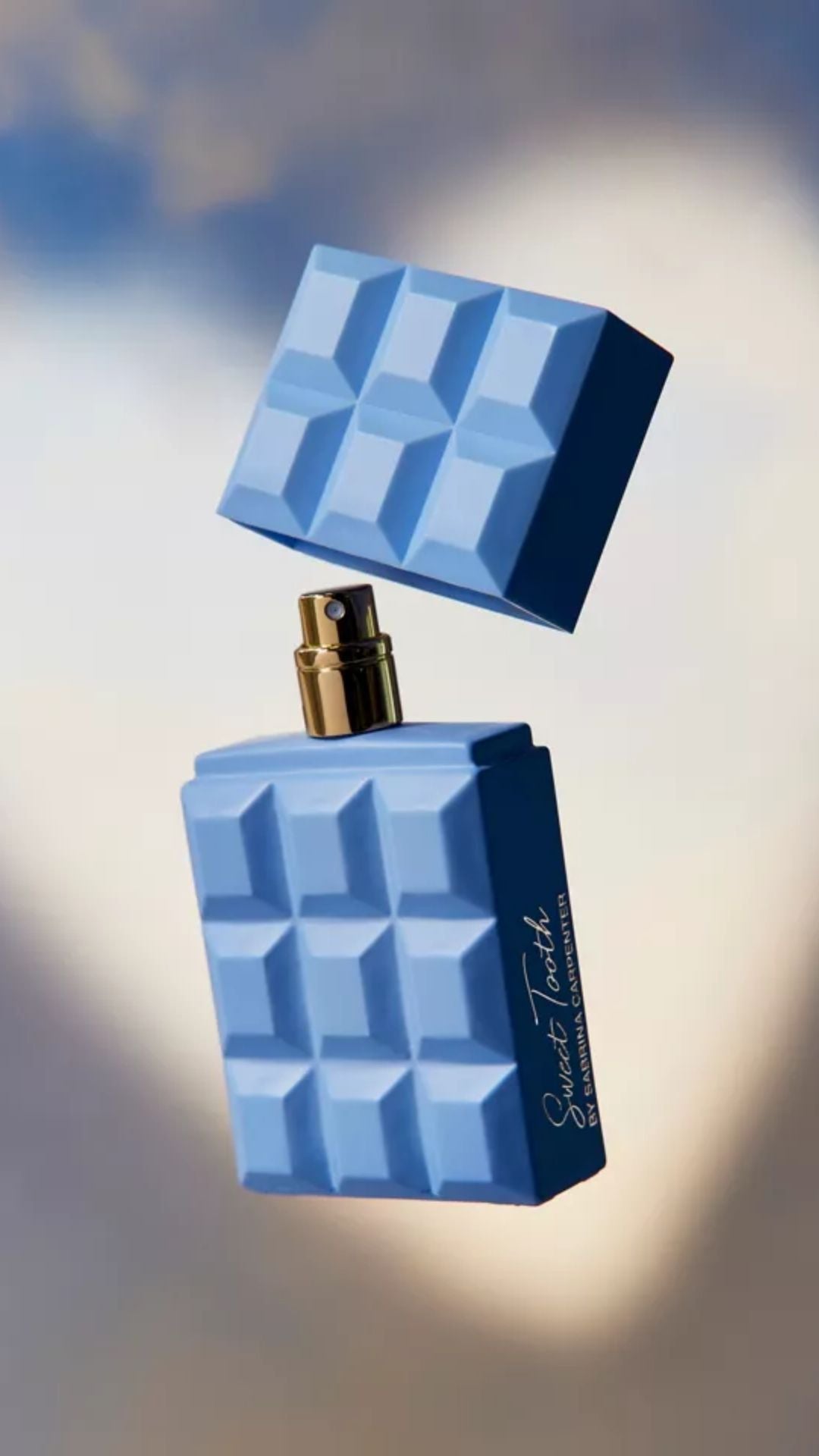 Blue geometric perfume bottle with gold cap against a blurred background