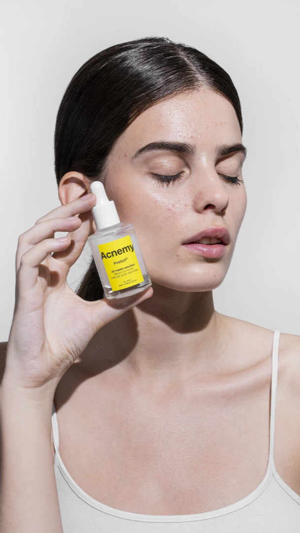 Woman holding a skincare serum bottle with a plain background