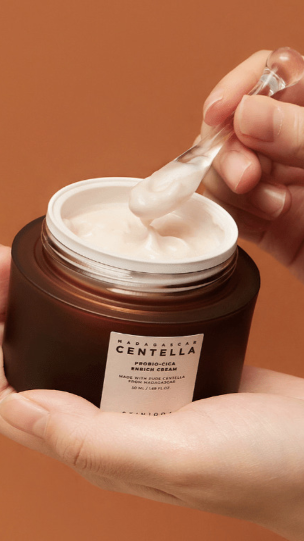 Hand holding a jar of cream with a spoonful being taken, against a brown background
