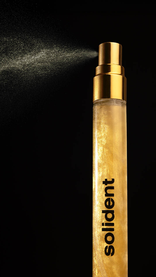 Wooden spray bottle with gold cap labeled 'solident' on a black background