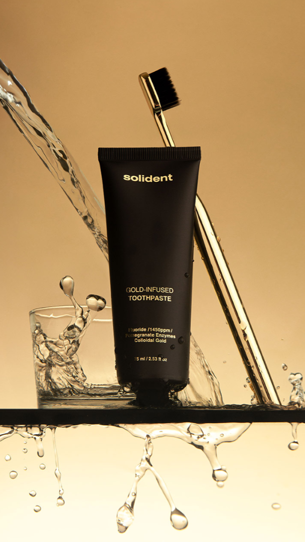 Black toothpaste tube labeled 'solident' with a gold toothbrush and water splash on a beige background