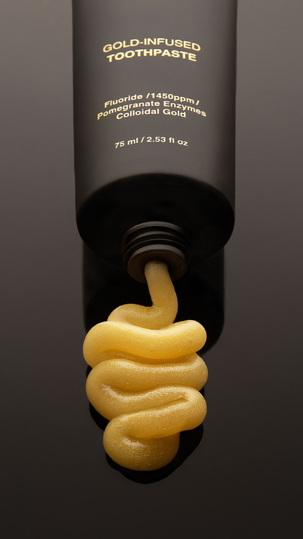 Gold-infused toothpaste being squeezed out of a black tube on a dark background