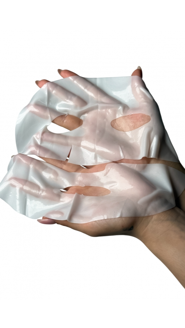 Hand holding a white sheet mask with pinkish hue on a white background