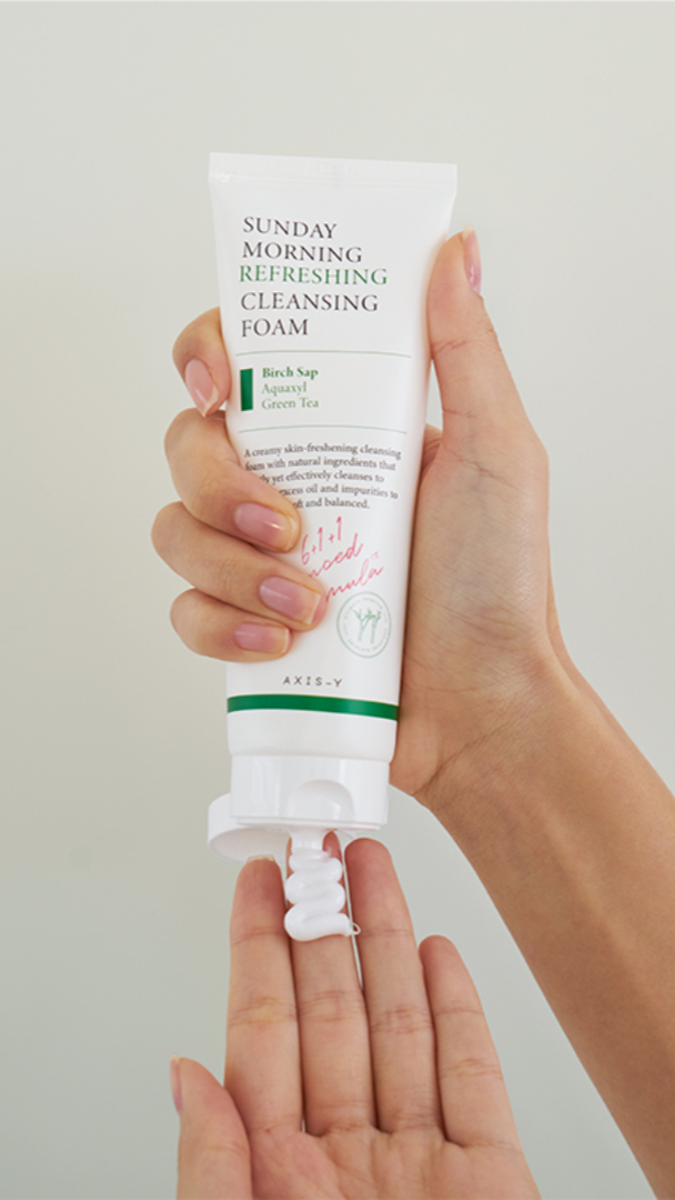 Hand holding a tube of Sunday Morning Refreshing Cleansing Foam against a light background