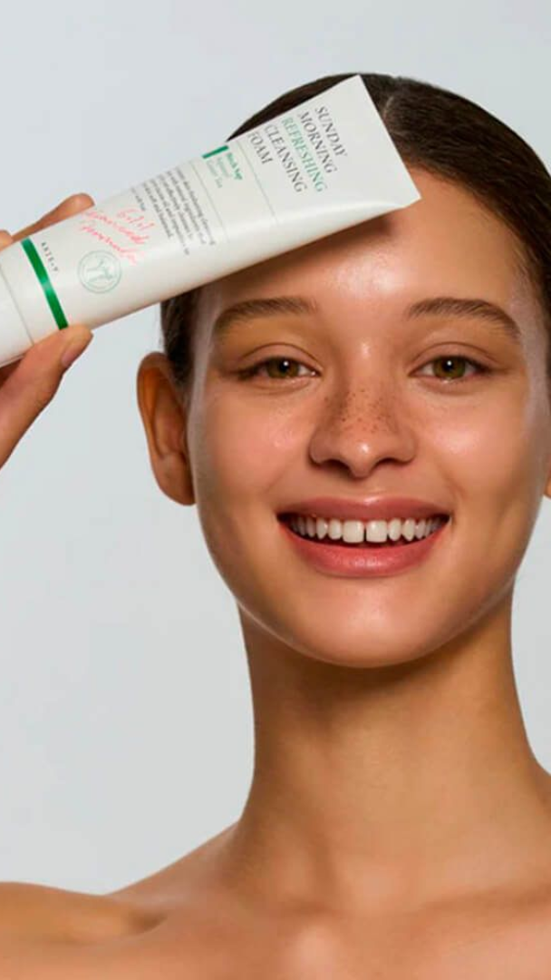 Woman applying sunscreen cream to her face with a plain background