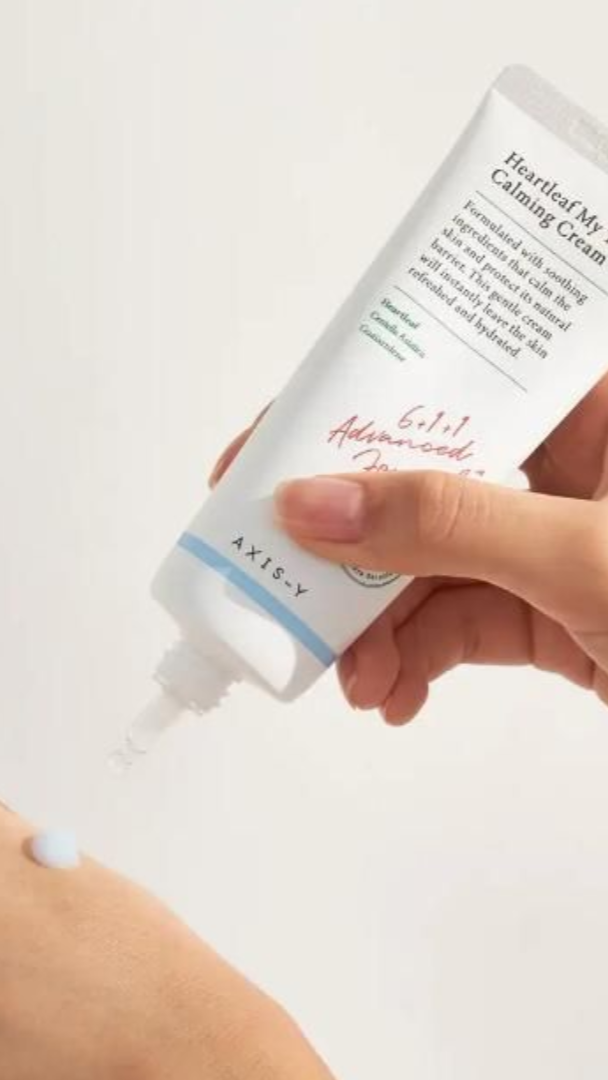 Hand holding a tube of AXIS-Y Calming Cream on a light background