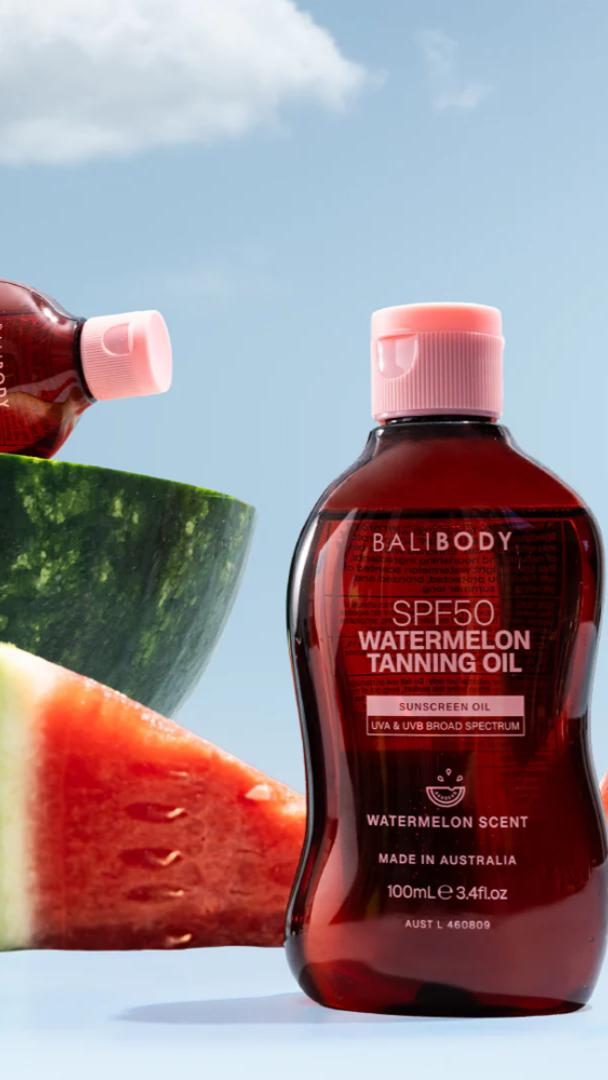 Bottle of Bali Body SPF50 Watermelon Tanning Oil with watermelon slices on a blue background