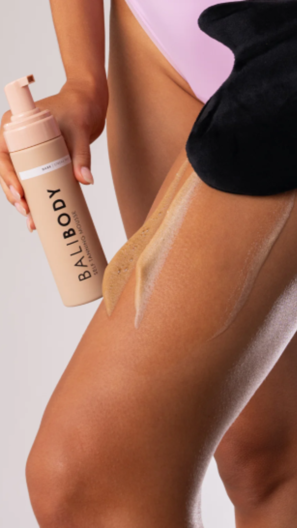 Person applying BaliBody tanning lotion to their leg with a clear background