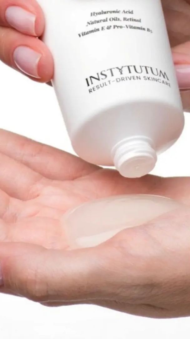 Hand holding a bottle of Instytutum skincare product with cream on palm