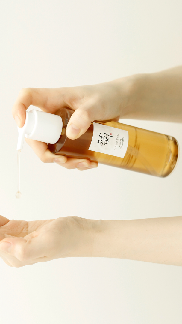 Hand holding a small bottle with a label, dispensing a clear liquid onto another hand against a light background.
