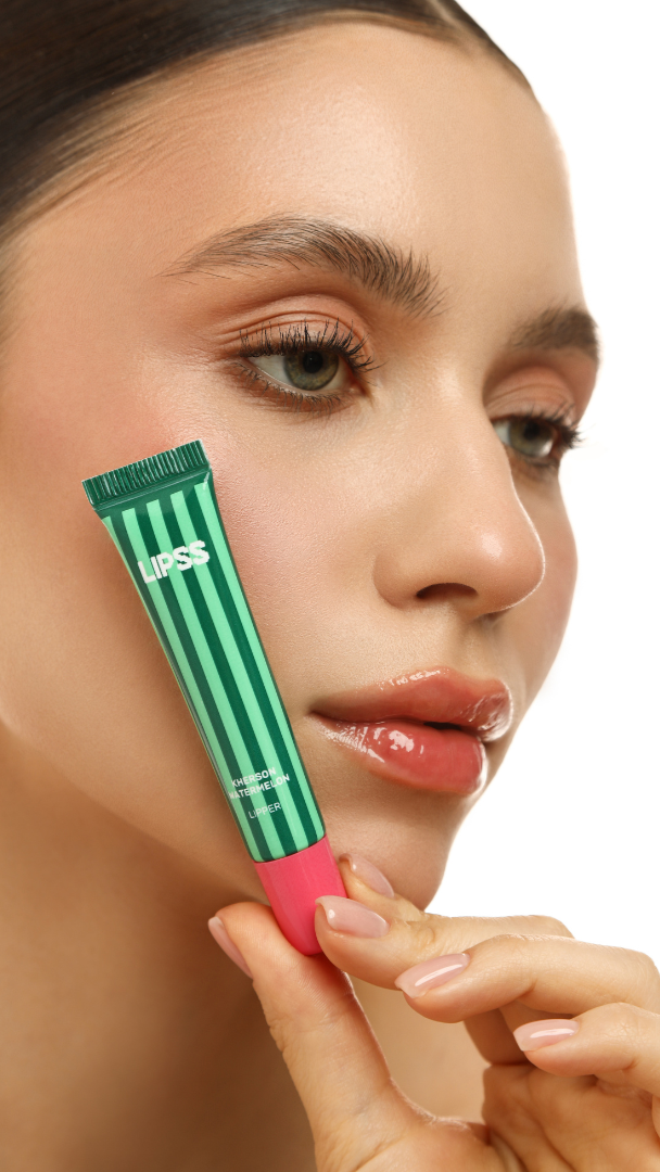 Woman holding a green and pink lip balm close to her face