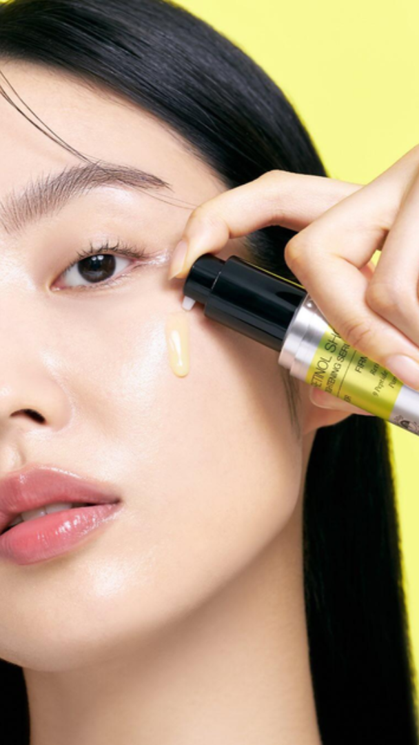Person applying makeup with a brush near their eye, against a yellow background