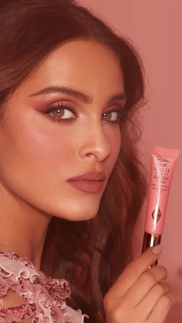 Woman holding a pink lip balm with a soft pink background