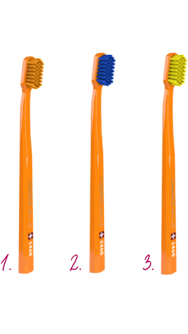 Three orange toothbrushes with different bristle colors on a white background